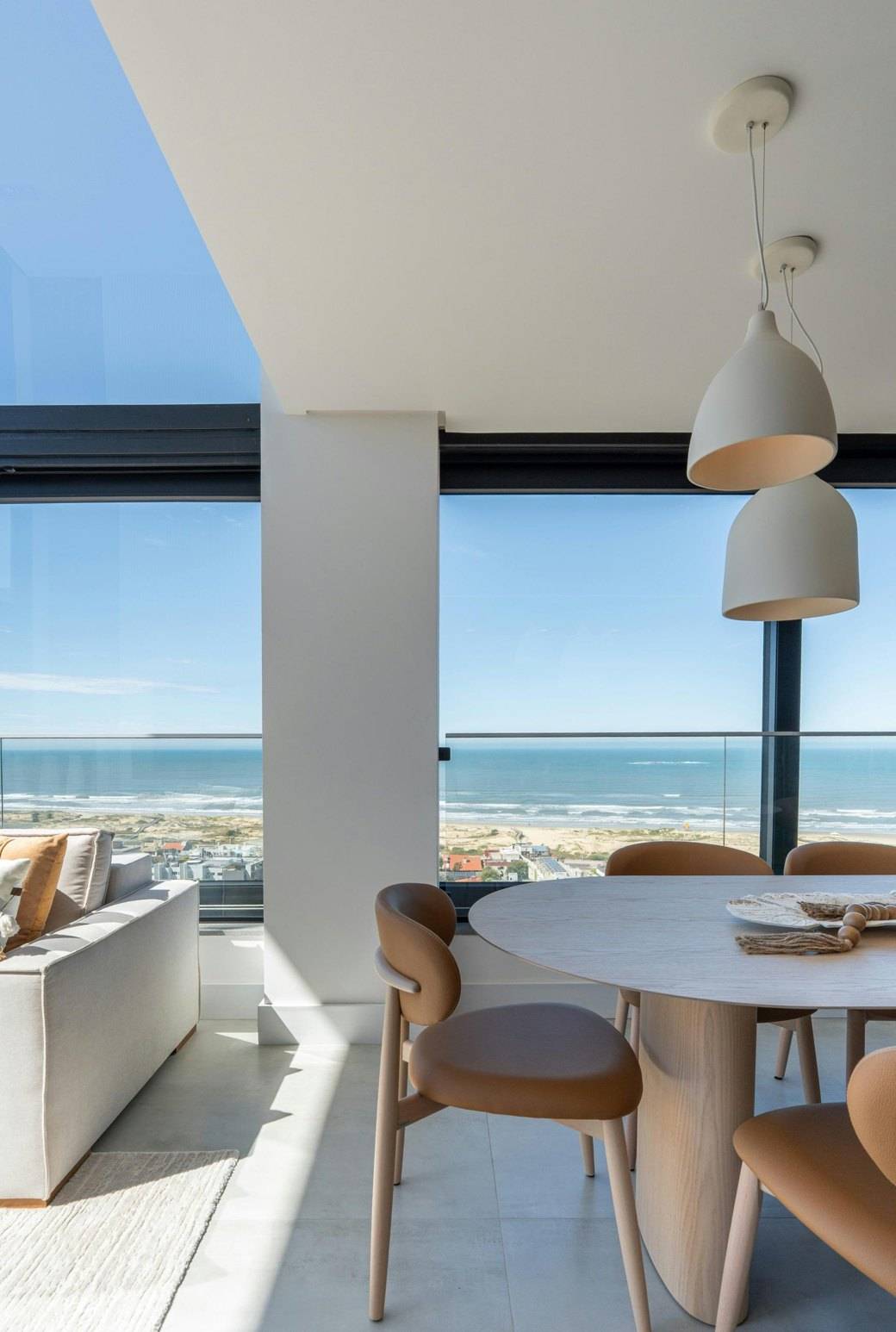 Séjour lumineux avec table en bois et grande baie vitrée ouverte sur la mer