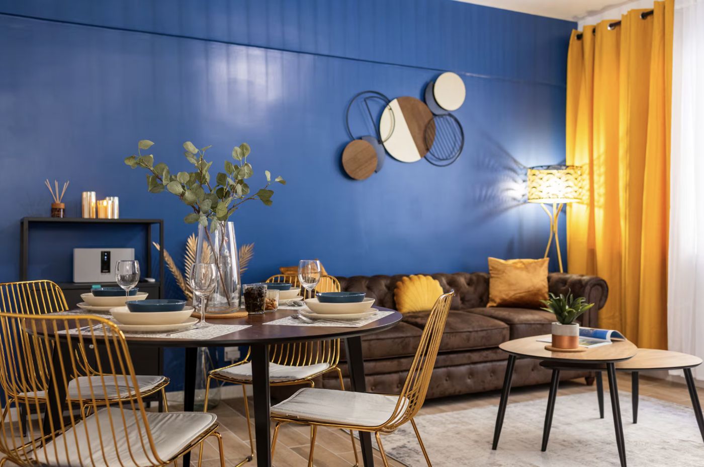 Séjour au mur bleu, table dressée et chaises dorées
