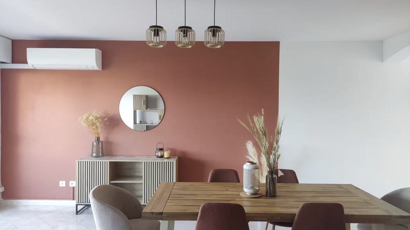 Salle à manger lumineuse au mur terracotta, table en bois et chaises velours