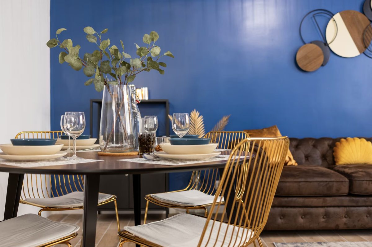 Table ronde dressée, chaises dorées et mur bleu, appartement géré par BOLIEUX à Toulon