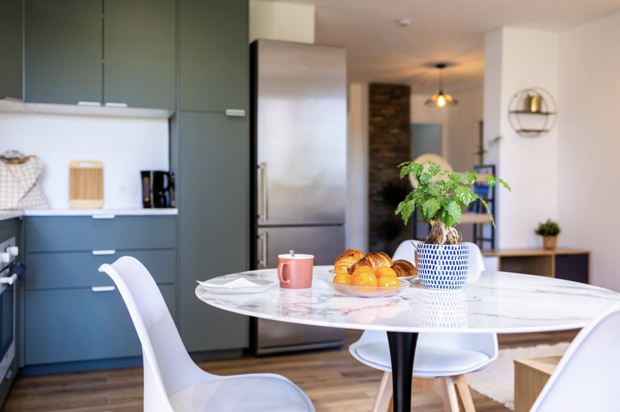 Table en marbre dressée pour le petit-déjeuner devant une cuisine vert de gris